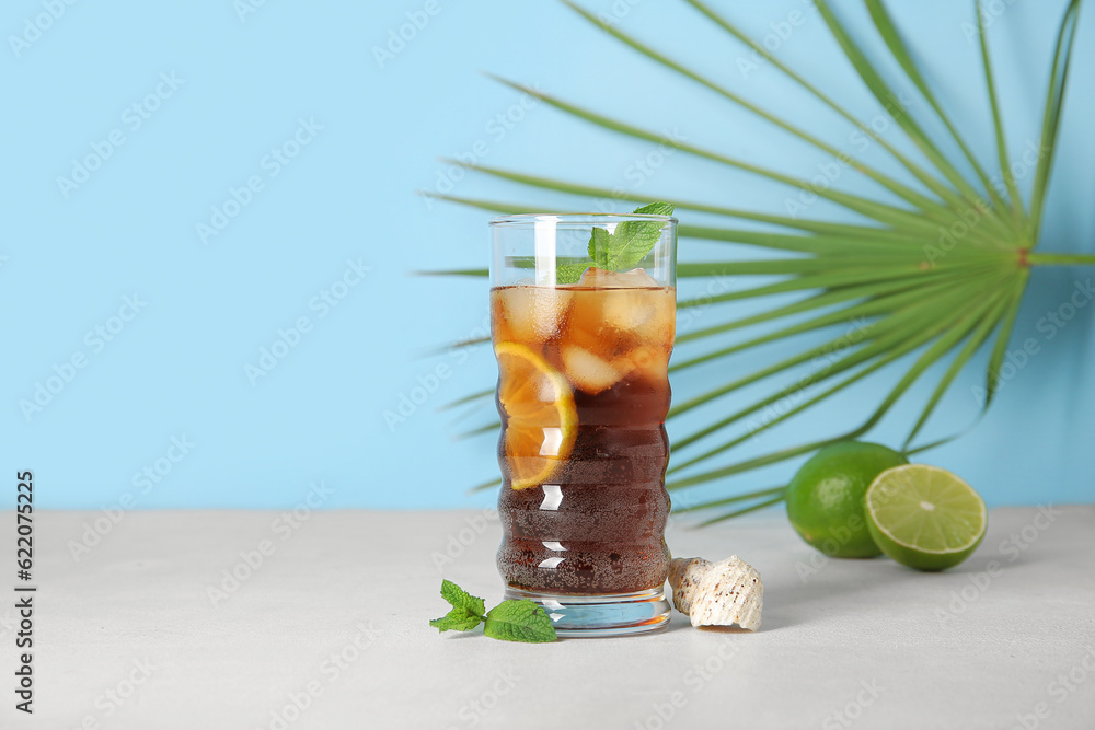 Glass of cold Cuba Libre cocktail, palm leaf and seashell on white table