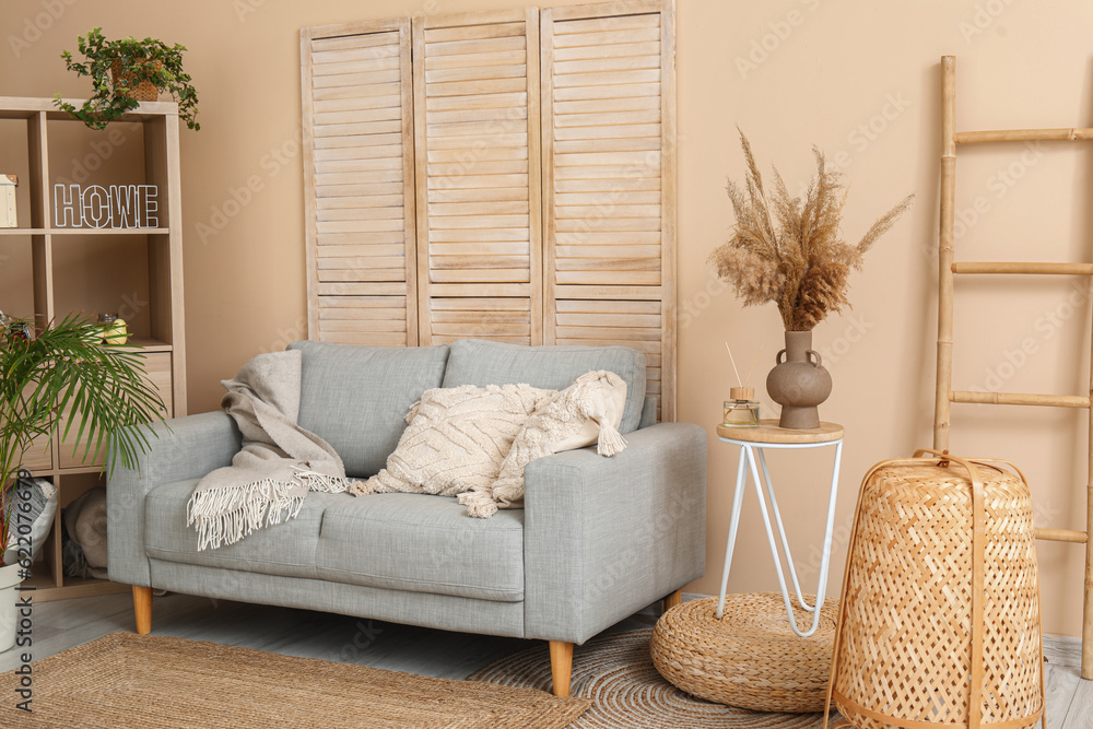 Interior of light living room with stylish grey sofa, shelving unit, folding screen and ladder