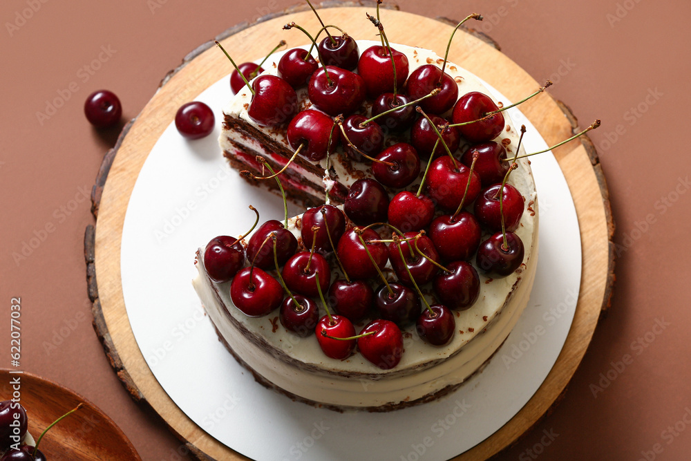 Wooden board with tasty cherry cake on brown background