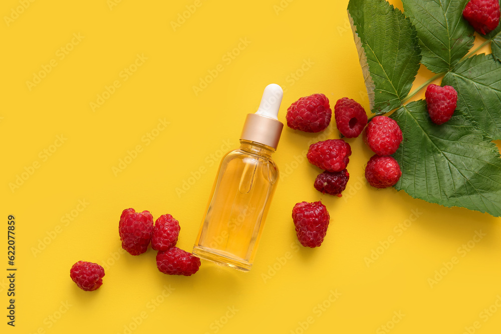 Bottle of cosmetic raspberry oil on yellow background