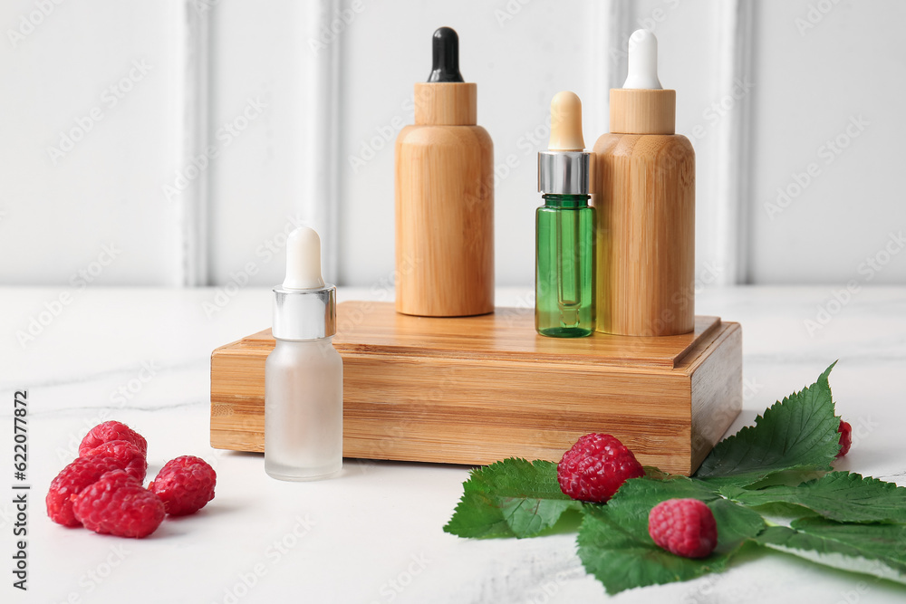 Wooden podium with bottles of cosmetic raspberry oil on white background