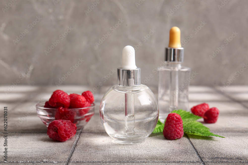 Bottles of cosmetic raspberry oil and bowl with berries on grey tile table