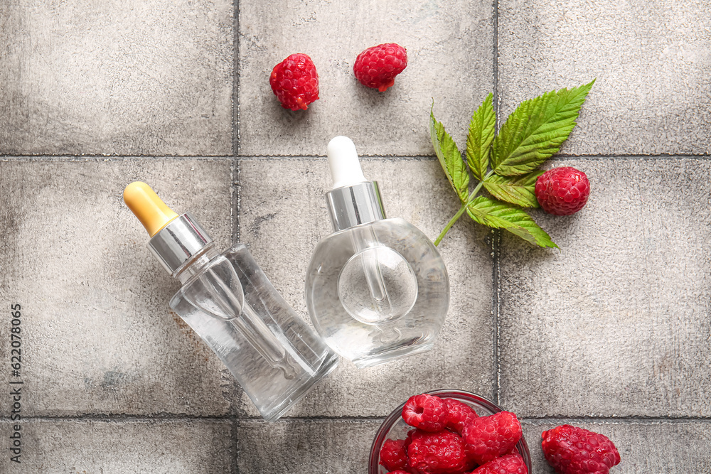 Bottles of cosmetic raspberry oil and bowl with berries on grey tile table