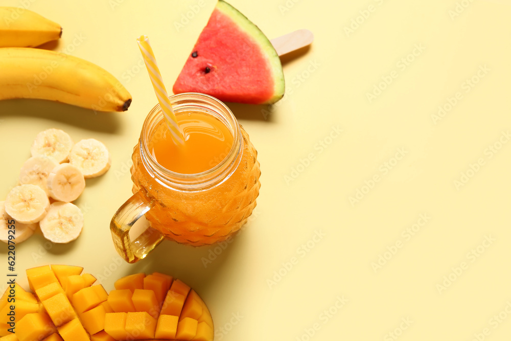 Mason jar of fresh mango juice with banana and watermelon on yellow background