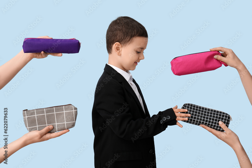 Cute little schoolboy and female hands with pencil cases on blue background