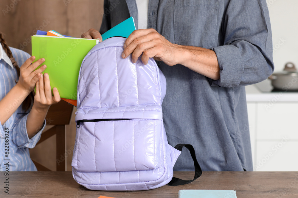 Father helping his little daughter to pack schoolbag in kitchen, closeup