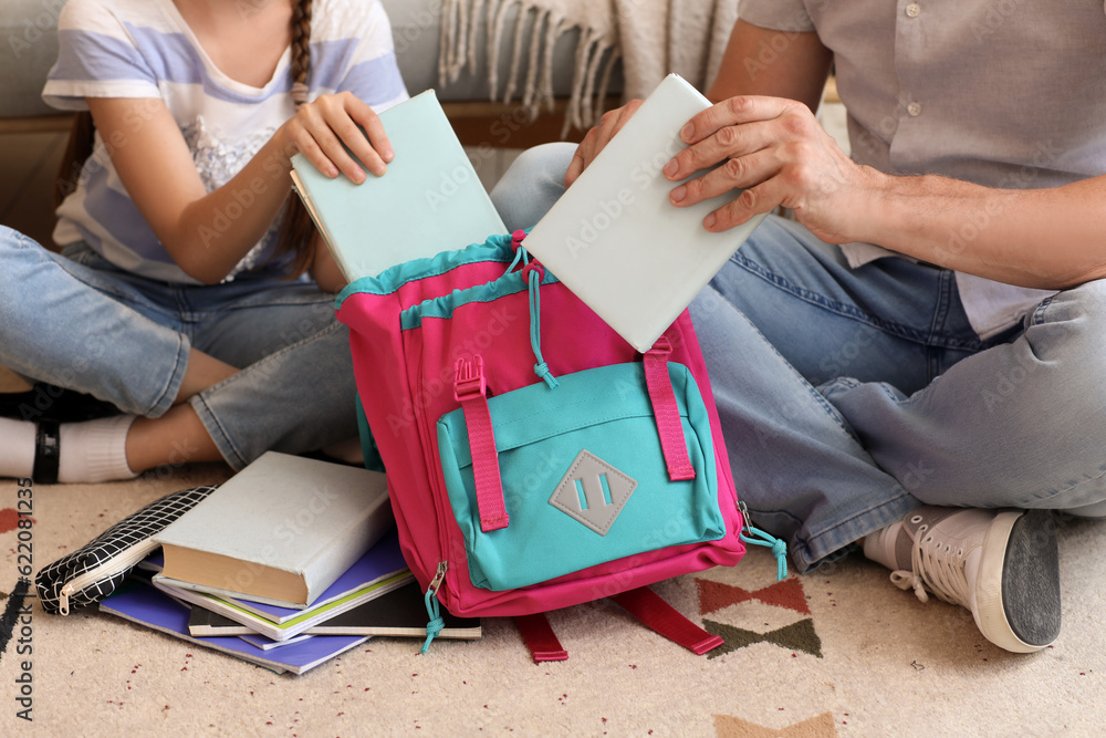 Father helping his little daughter to pack schoolbag at home