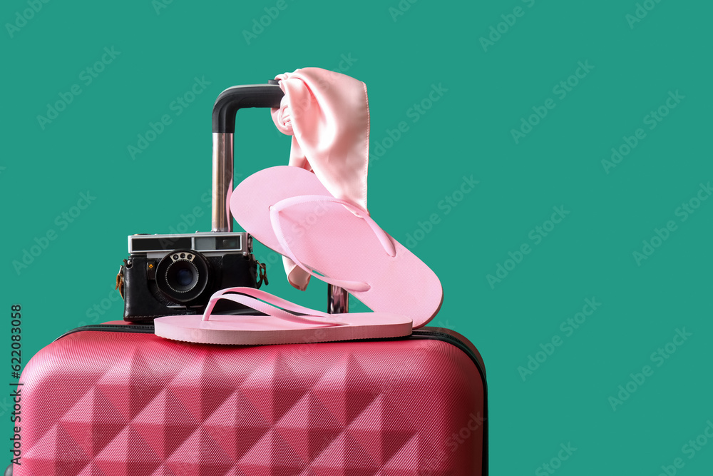 Suitcase with flip flops and camera on turquoise background. Travel concept