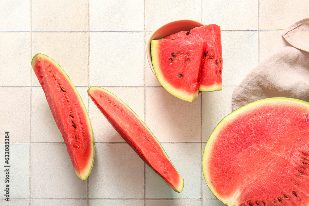 Half of fresh watermelon and bowl with pieces on white tile background