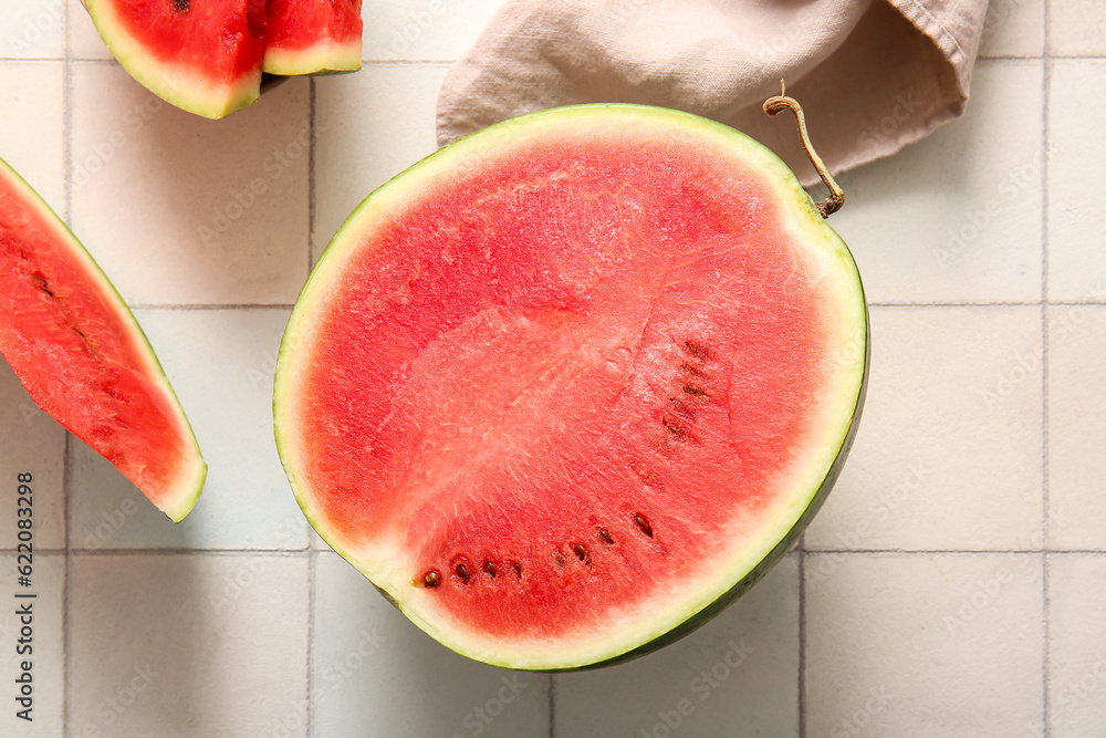 Half of fresh watermelon with pieces on white tile table