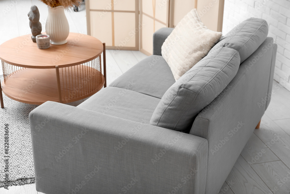 Cozy grey sofa with pillow and coffee table near white brick wall