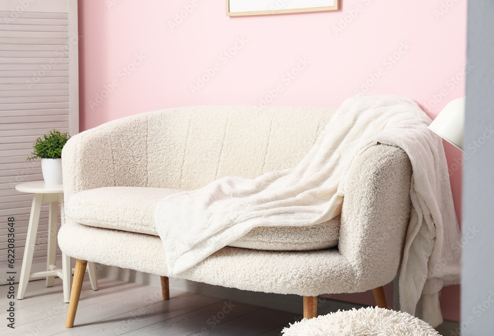 Cozy white sofa and blanket near pink wall