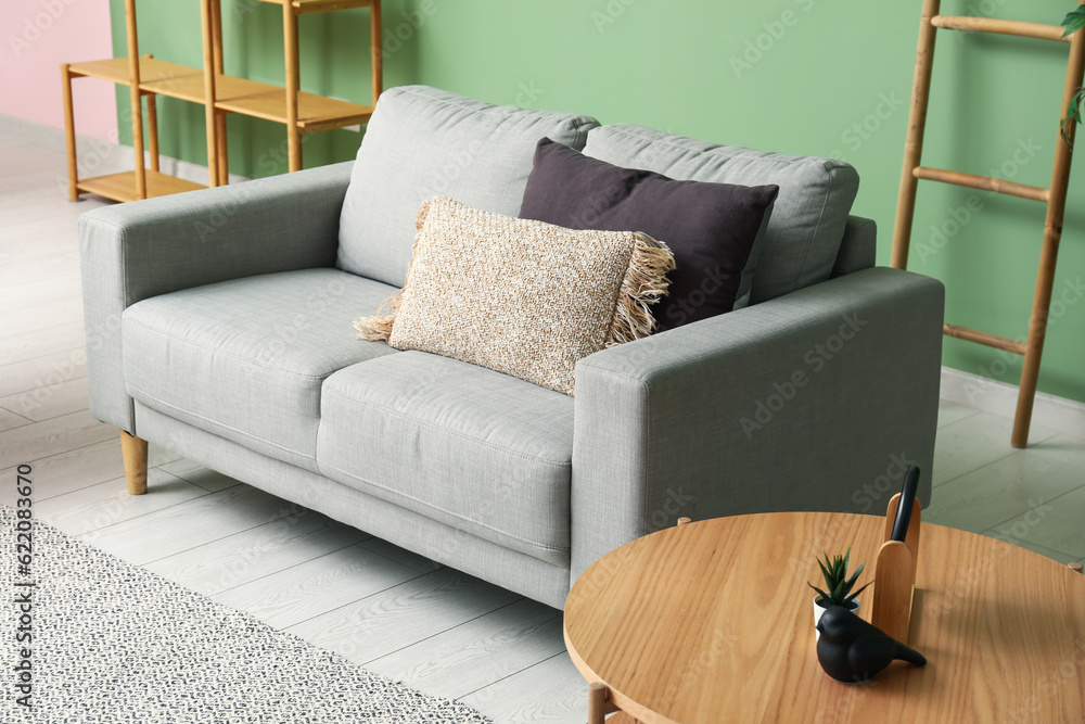 Cozy grey sofa with pillows and coffee table near green wall