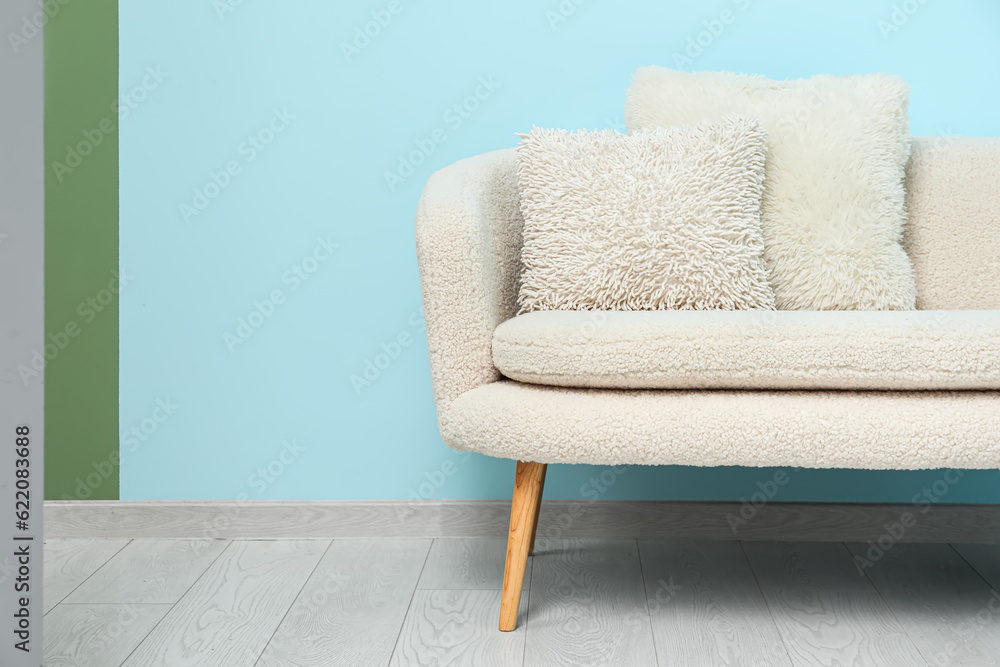 Cozy white sofa with pillows near blue wall