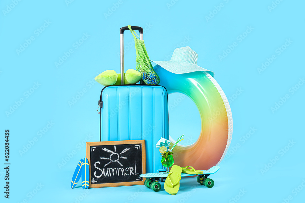 Suitcase, beach accessories and blackboard with word SUMMER on blue background. Travel concept