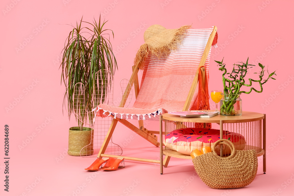 Deckchair with table and beach accessories on pink background. Travel concept