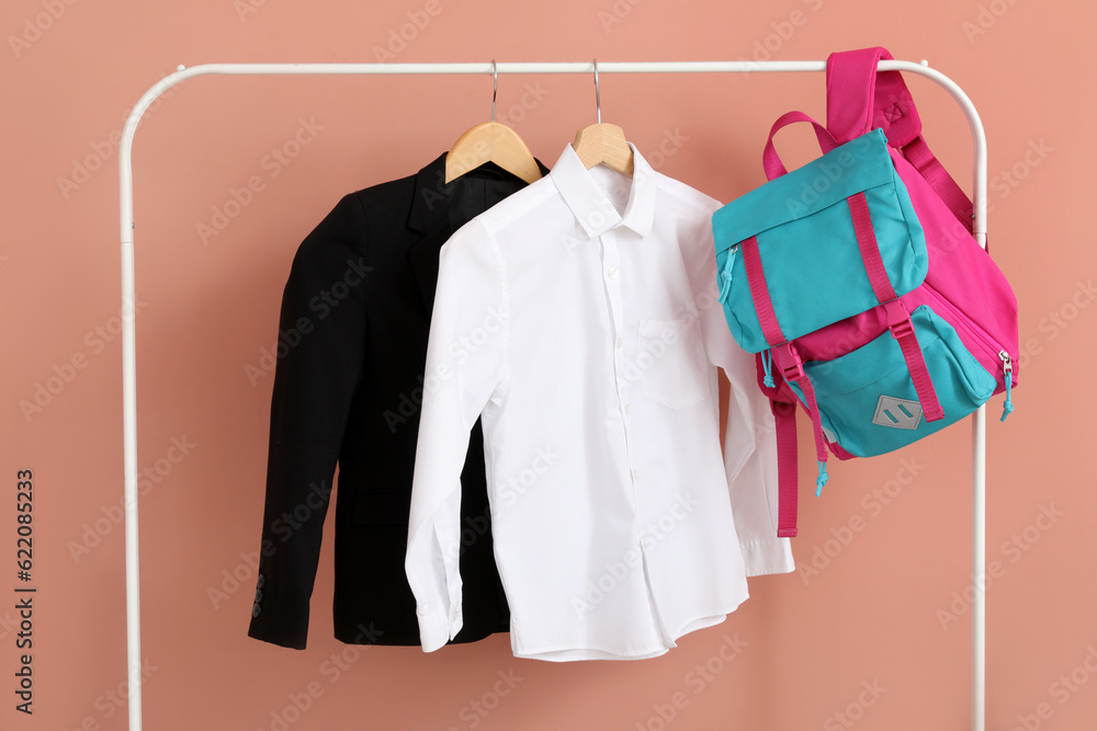 Rack with stylish school uniform and backpack near beige wall in room