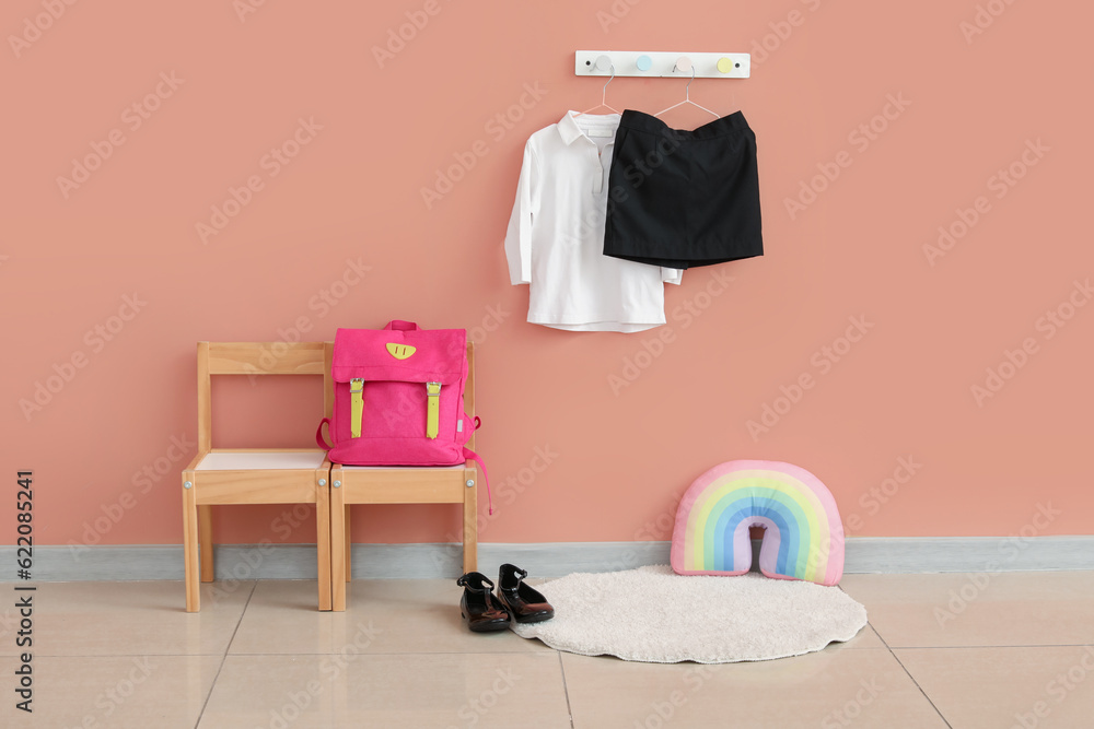 Chairs with backpack, shoes and stylish school uniform hanging on beige wall in room