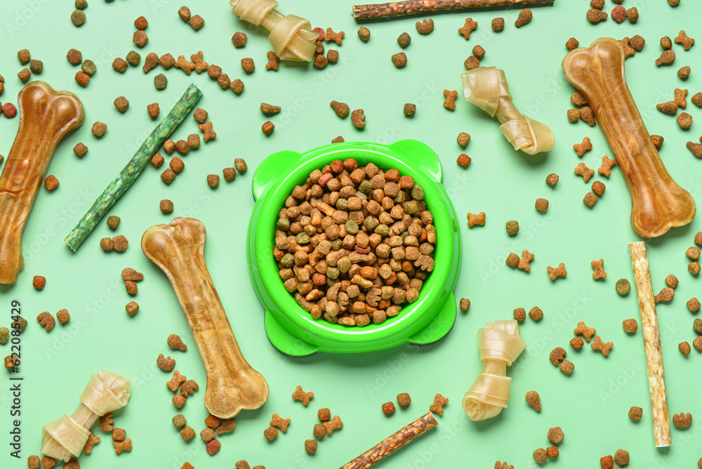 Composition with bowl of dry dog food and treats on color background