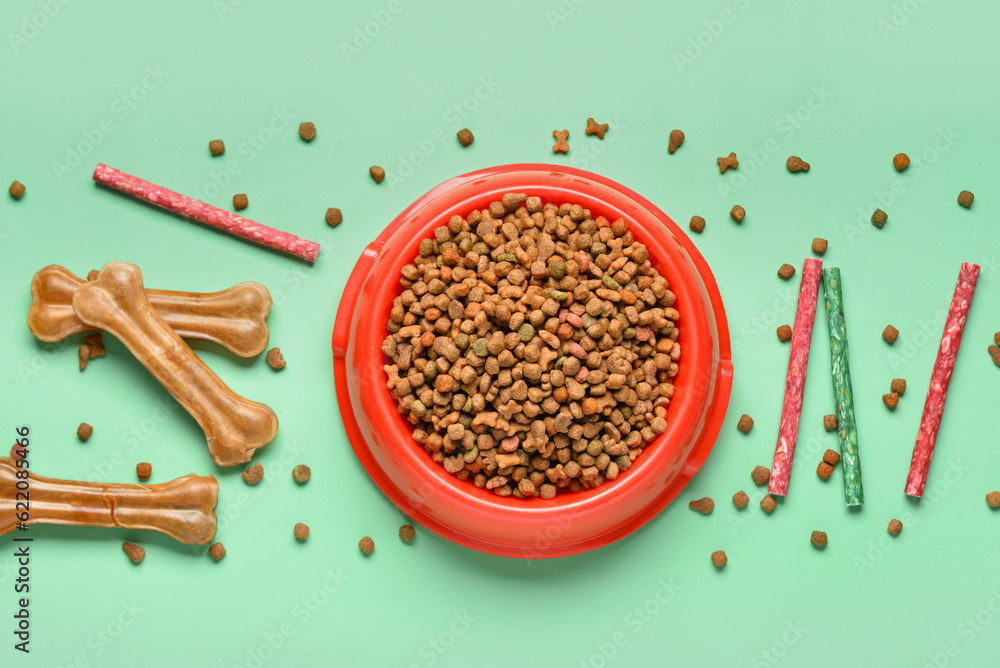 Composition with bowl of dry dog food and snacks on color background