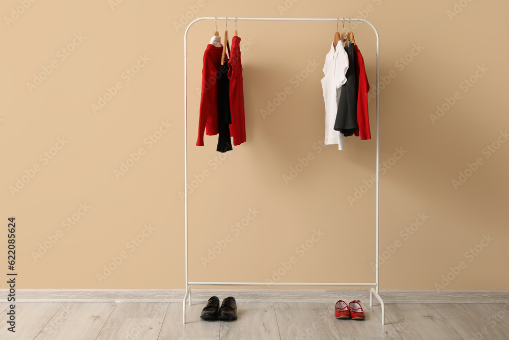 Rack with stylish school uniform and shoes near color wall