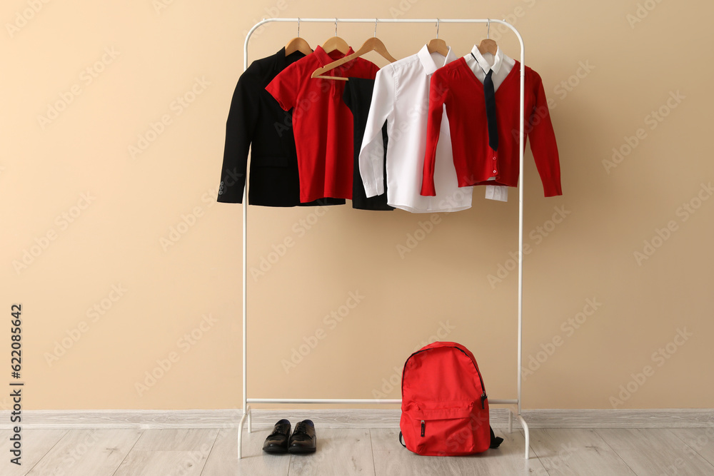 Rack with stylish school uniform, backpack and shoes near color wall