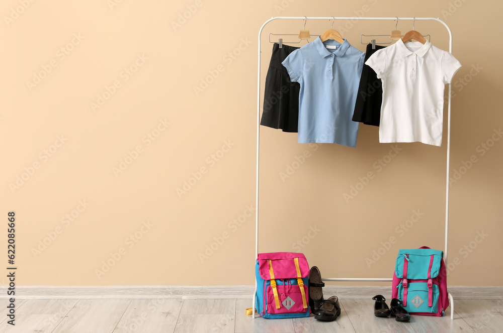 Rack with stylish school uniform, backpacks and shoes near color wall