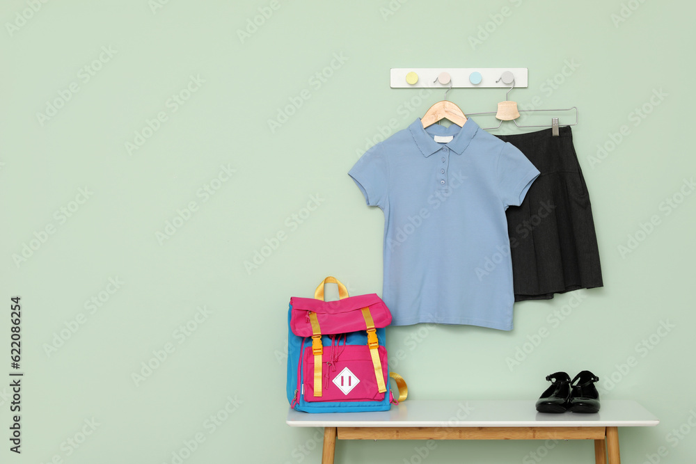 Table with school backpack, shoes and uniform hanging on color wall