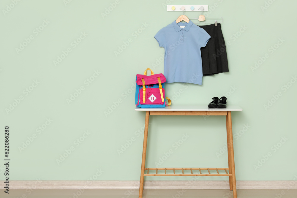 Table with school backpack, shoes and uniform hanging on color wall