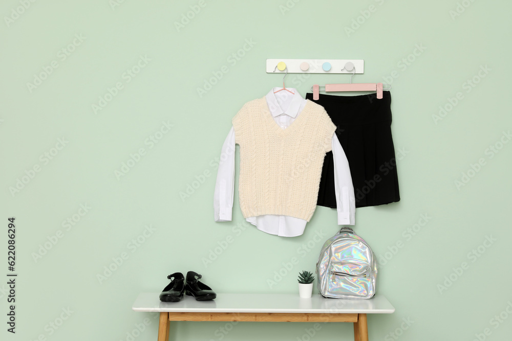 Stylish school uniform hanging on color wall, shoes and backpack