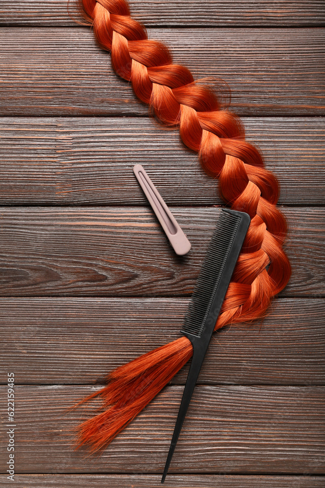 Braided ginger hair, comb and clip on wooden background