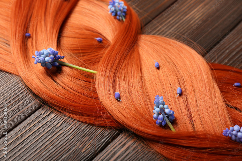 Beautiful ginger hair with Muscari flowers on wooden background, closeup