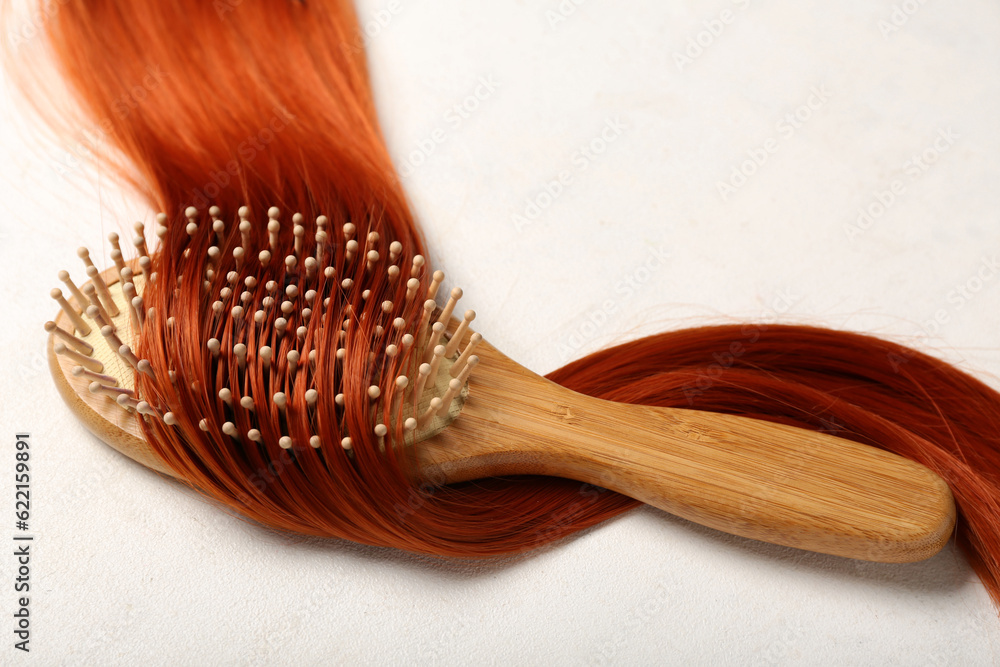 Ginger hair strand with brush on light background, closeup