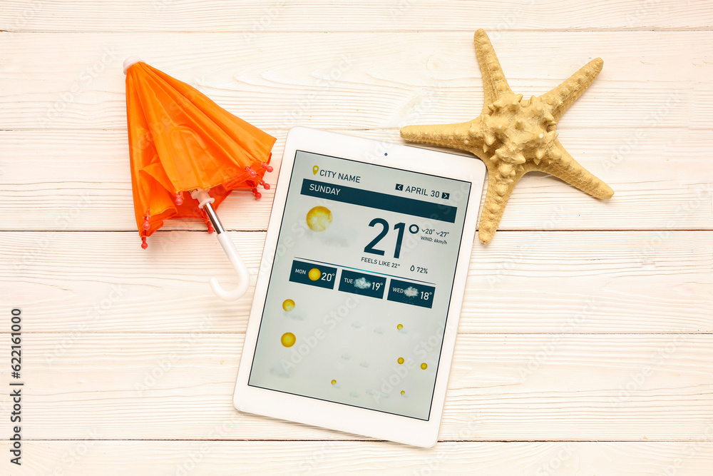 Tablet computer with weather forecast, umbrella and starfish on white wooden background