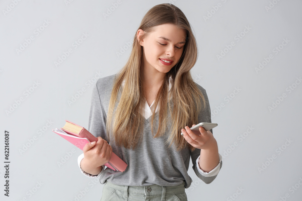 Happy female student with mobile phone, notebooks and book on grey background