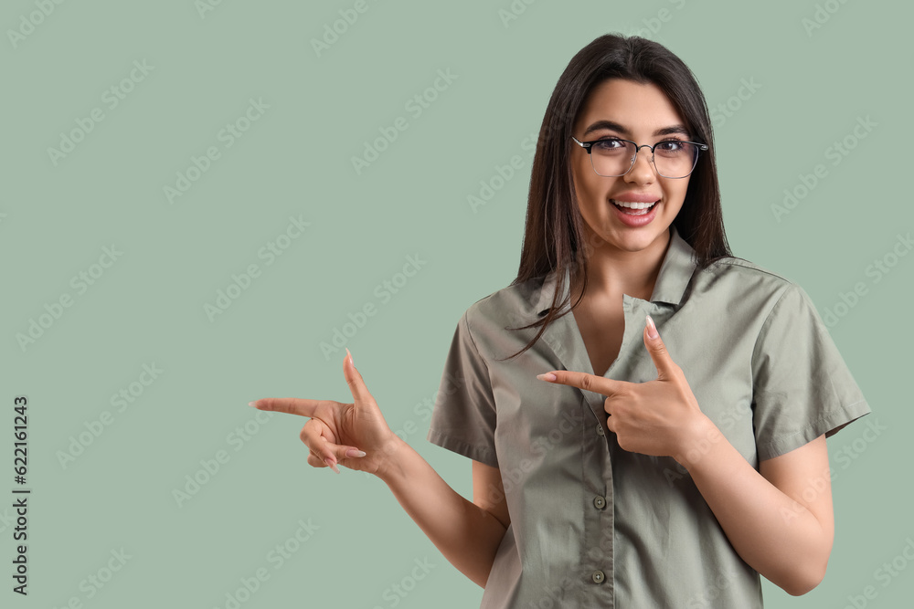 Beautiful young woman wearing glasses and pointing at something on color background