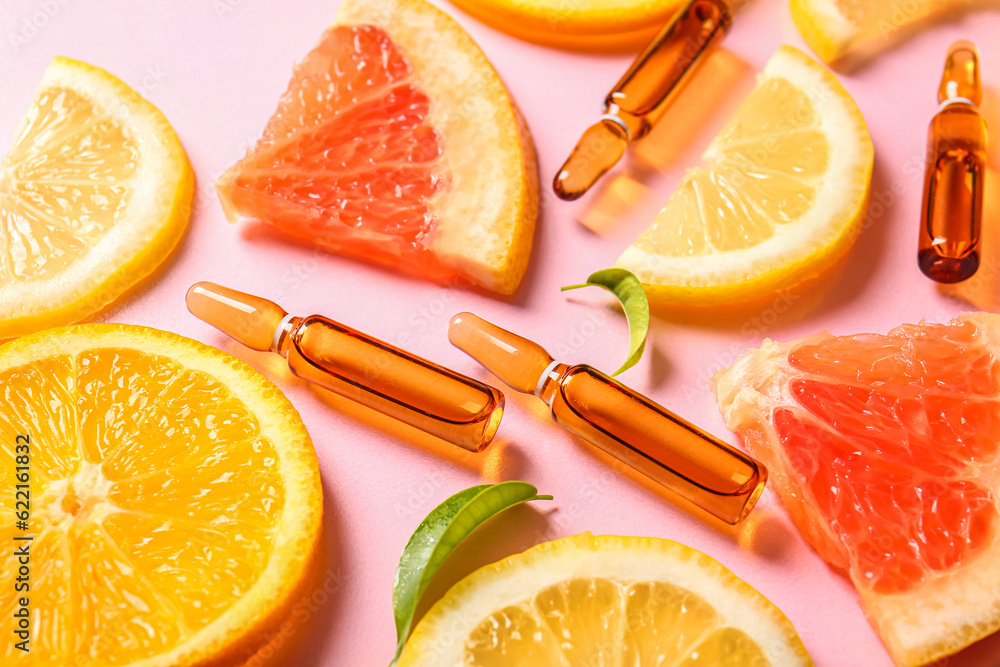 Ampoules with vitamin C and different citrus fruit slices on pink background