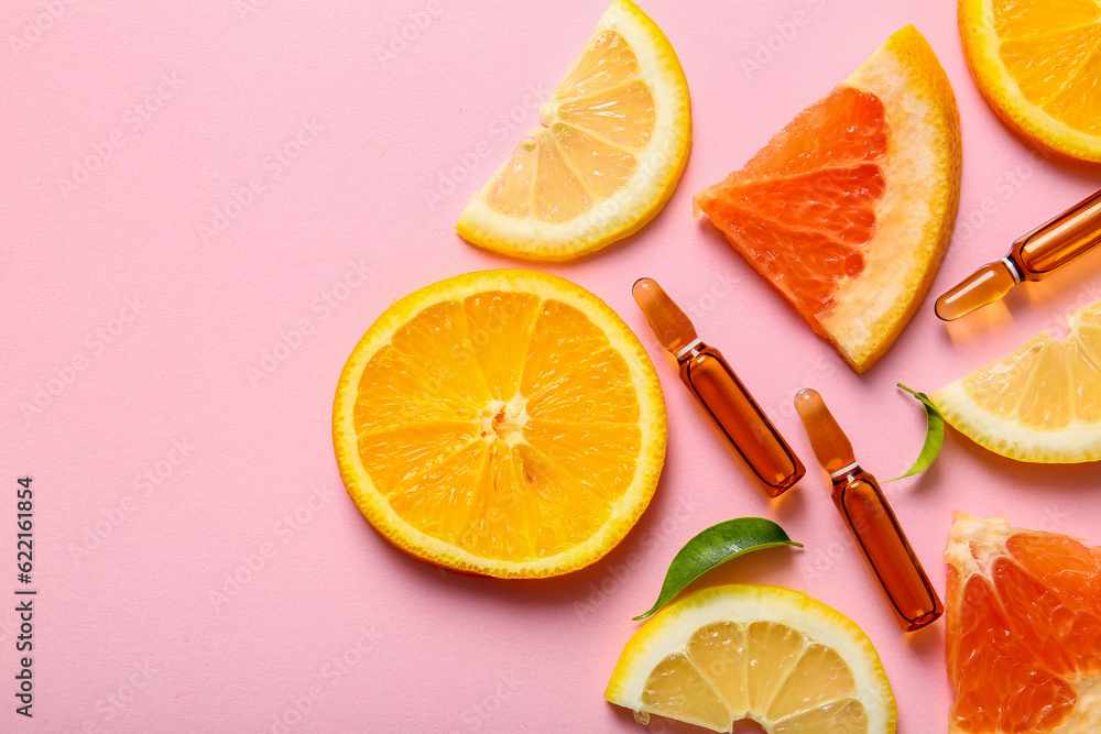 Ampoules with vitamin C and different citrus fruit slices on pink background