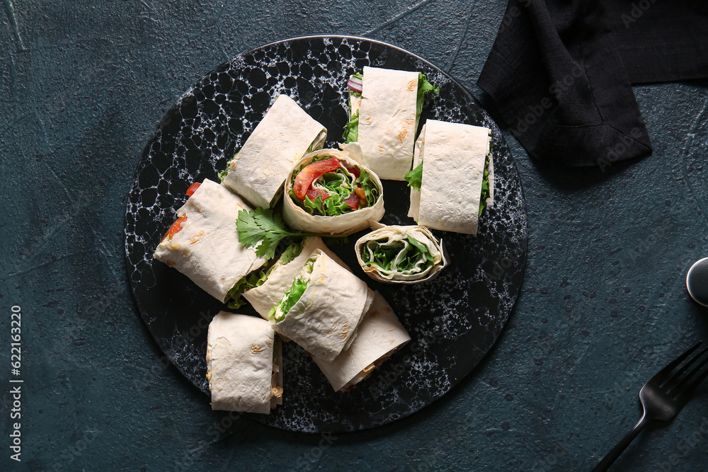 Board of tasty lavash rolls with vegetables and greens on black background