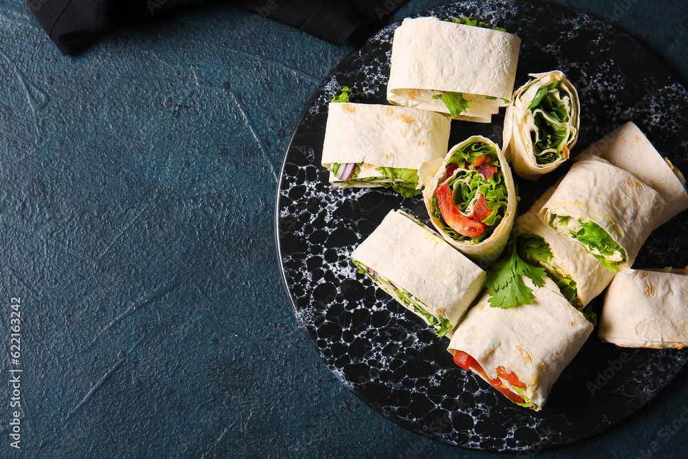 Board of tasty lavash rolls with vegetables and greens on black background