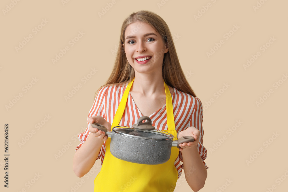 Young woman with cooking pot on beige background