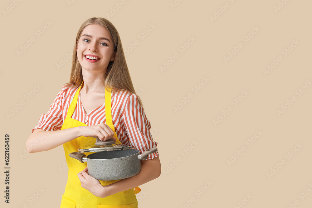 Young woman with cooking pot on beige background