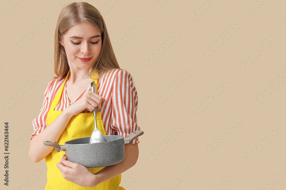 Young woman with cooking pot on beige background