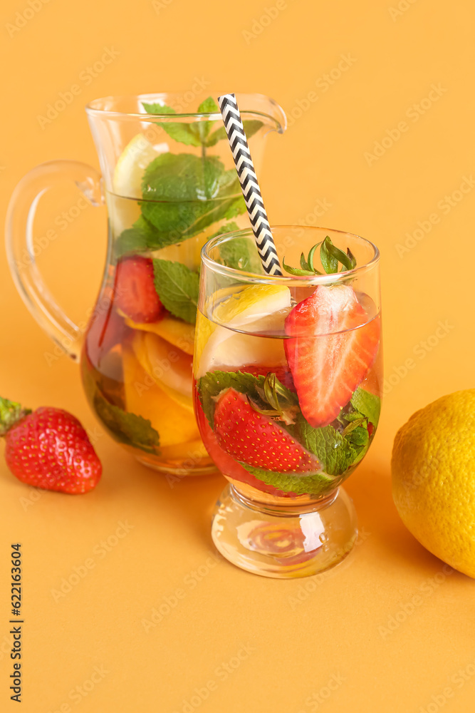 Glass and jug of fresh lemonade with strawberry on orange background