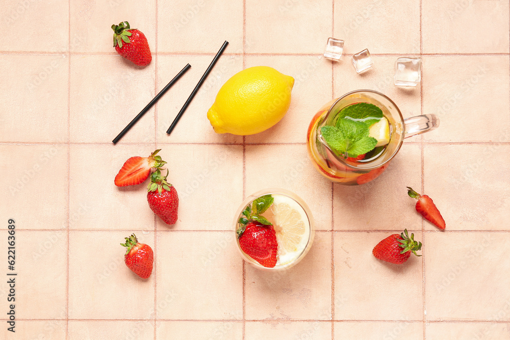 Glass and jug of fresh lemonade with strawberry on pink tile background