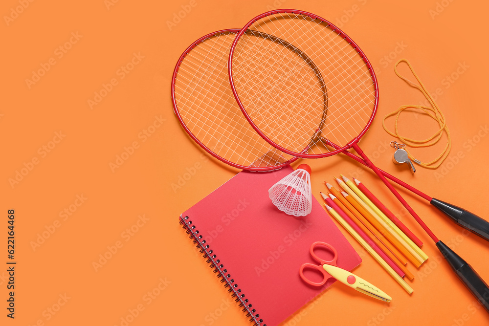 Rackets with badminton shuttlecock, whistle and different stationery on orange background