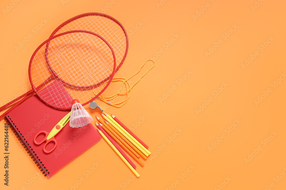 Rackets with badminton shuttlecock, whistle and different stationery on orange background