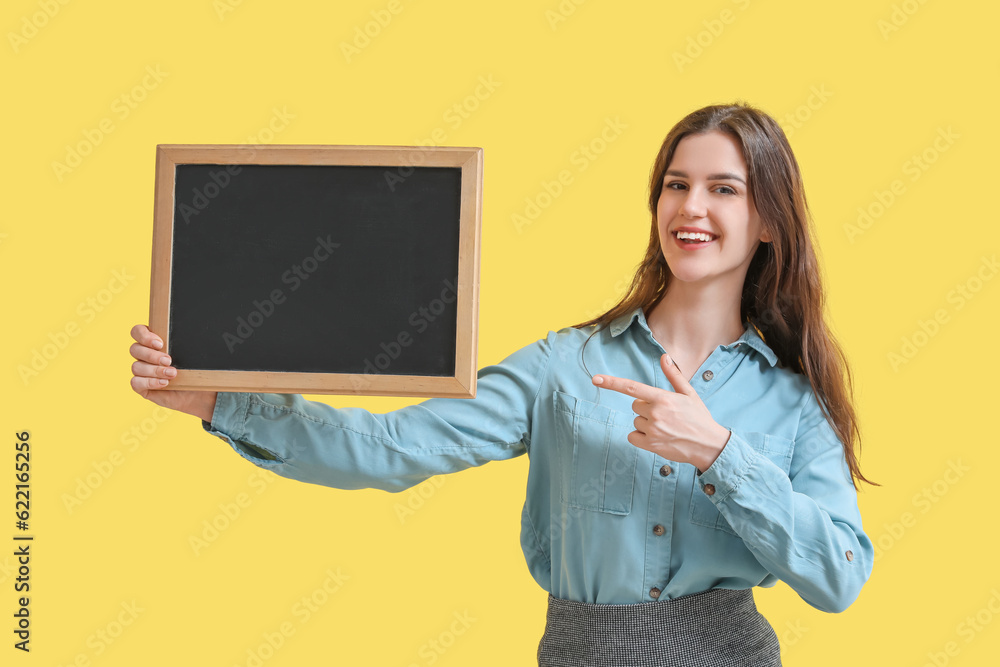 Female teacher pointing at chalkboard on yellow background