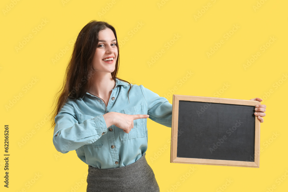 Female teacher pointing at chalkboard on yellow background