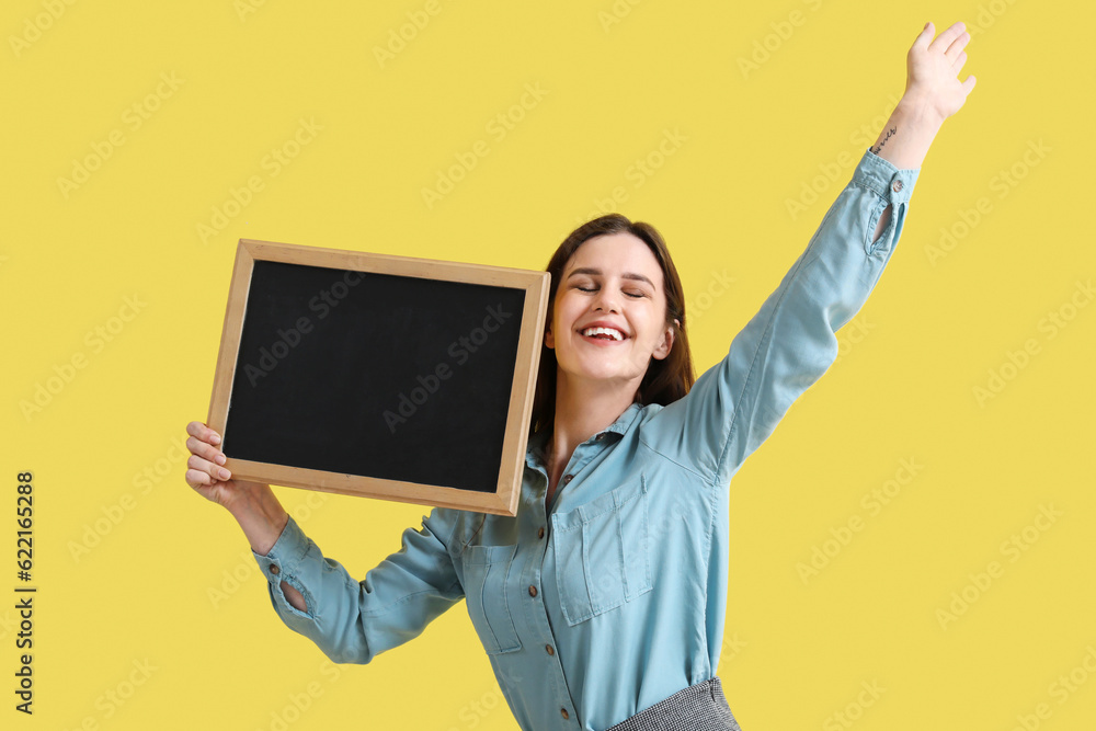 Happy female teacher with chalkboard on yellow background